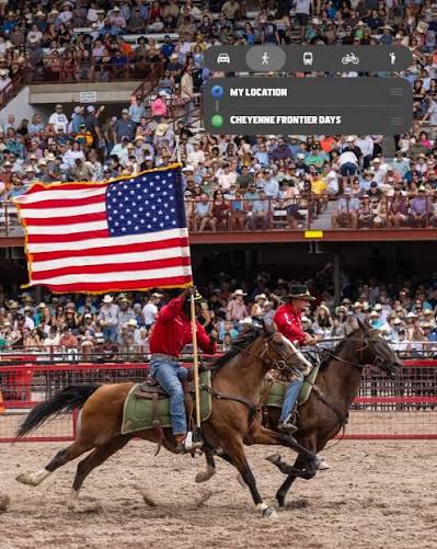 Riders on galloping horses carry a large American flag in a rodeo arena as a cheering crowd watches.