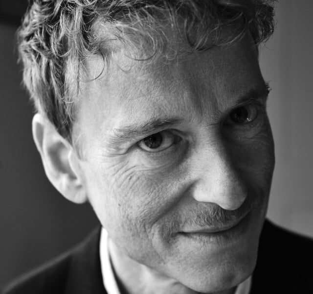 Close-up black-and-white portrait of a man, showing his eye and hair with a hint of mustache, wearing a collared shirt and suit.