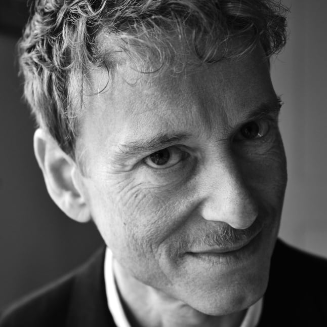 Close-up black-and-white portrait of a man, showing his eye and hair with a hint of mustache, wearing a collared shirt and suit.